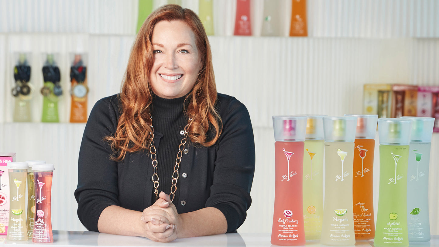 Julie Stevens, the founder and CEO of BeTini Spirits standing next to bottles of different flavors of BeTini.